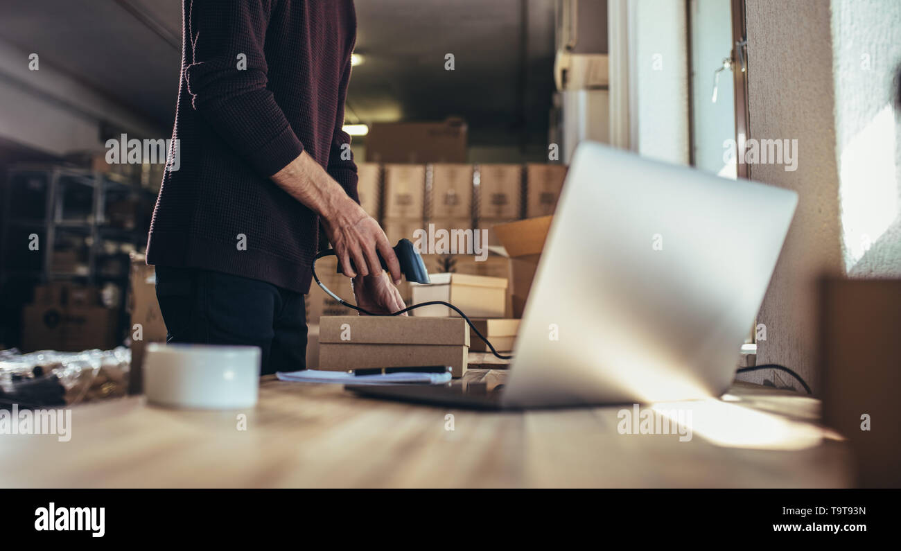 7/8 Schuß des Menschen Scannen des Barcodes der Sendung an seinem Schreibtisch. Mann bei der Arbeit in einem Drop Shipping Office, ein Paket an den Kunden zu liefern Stockfoto