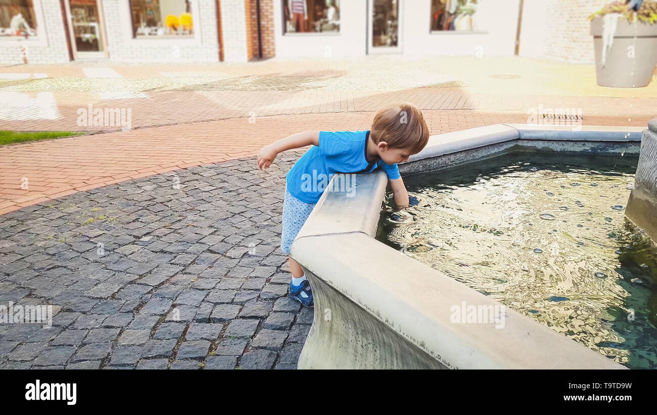 Portrait von adorable 3 Jahre altes Kleinkind junge berühren Wasser in Brunnen im Park Stockfoto