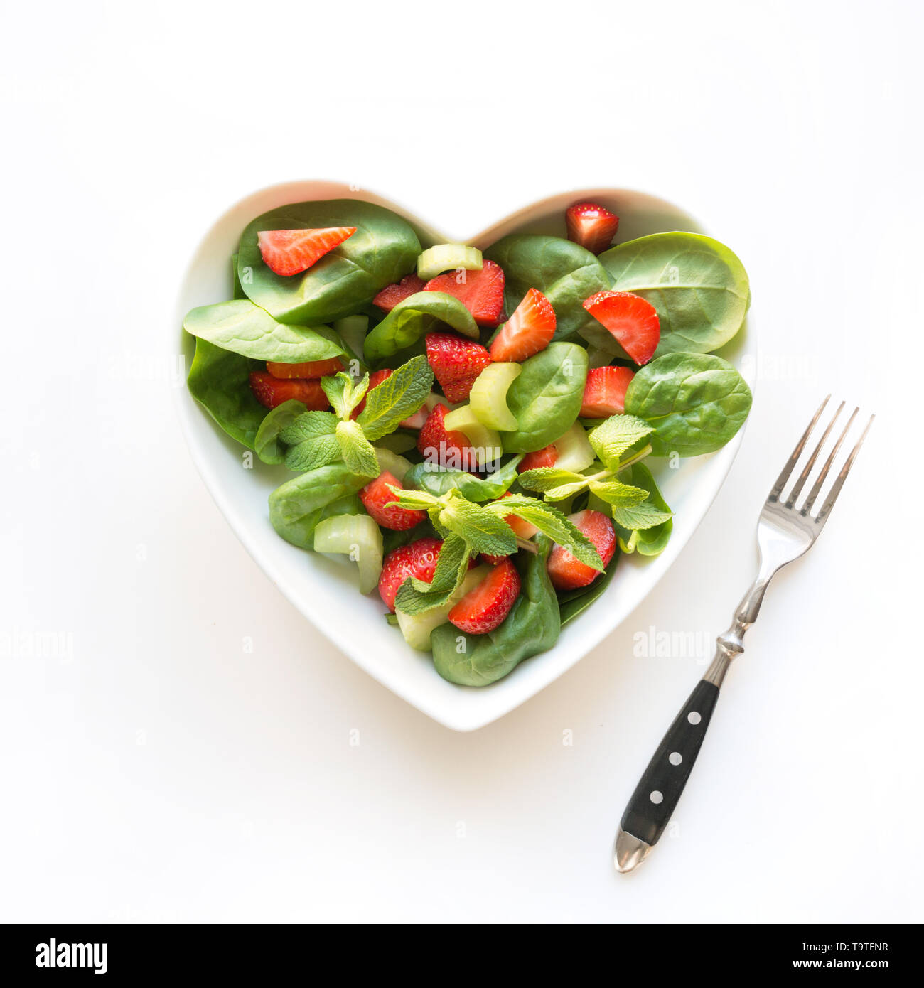 Frischer Salat von Erdbeere, Sellerie, Spinat, Pinienkerne, Käse in der Platte als Herzen auf Weiß. Konzept sauber, Essen für die Entgiftung. Blick von oben. Stockfoto