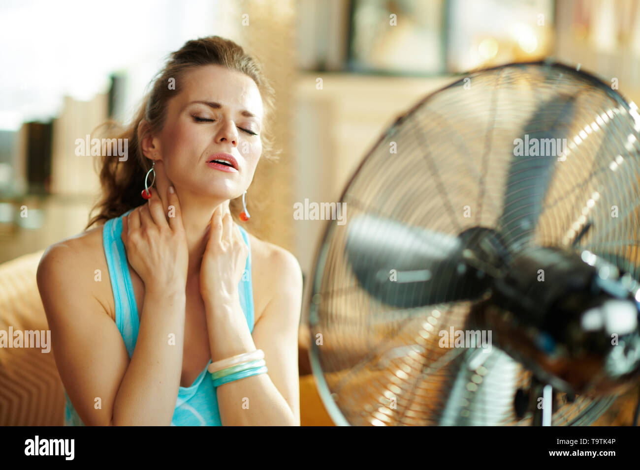 Entspannt junge Frau in der modernen Wohnzimmer im sonnigen heißen Sommertag Abkühlung an der Vorderseite des Lüfters Leiden von der Sommerhitze. Stockfoto