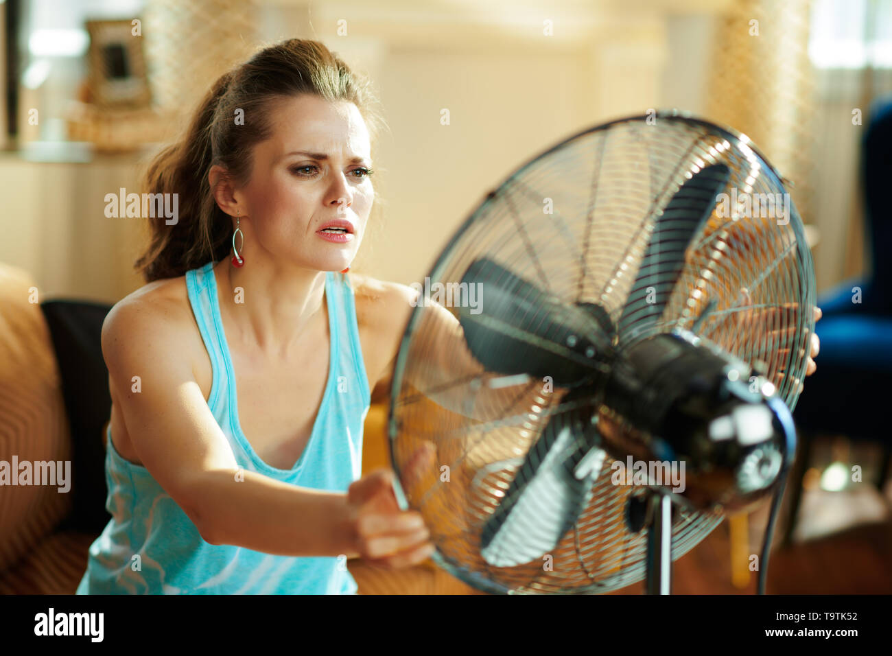 Heiße Hausfrau in der modernen Wohnzimmer im sonnigen heißen Sommertag mit Sieg Geste ab Sommer Hitze leiden. Stockfoto