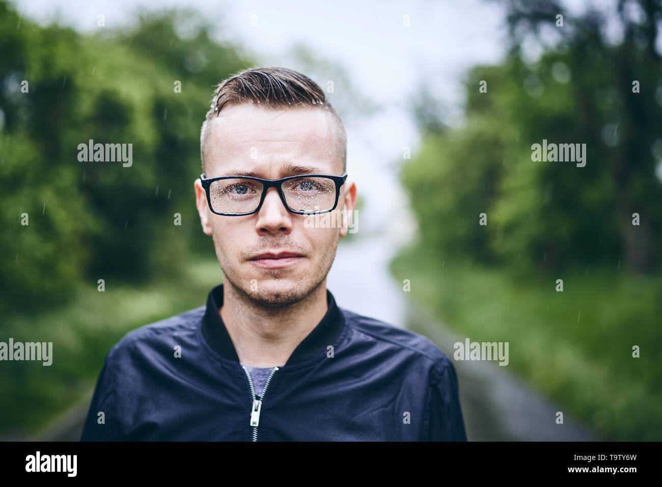 Porträt eines jungen Mannes mit Brillen in Regen. Selektiver Fokus auf Regentropfen. Stockfoto