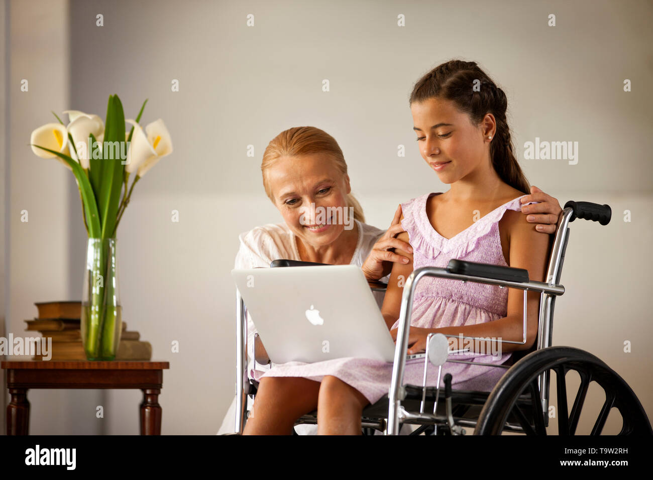 Reife Frau kniet neben ihrer Enkelin, der sitzt im Rollstuhl. Stockfoto