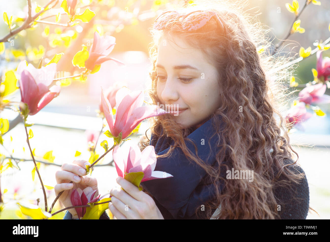 Junge Frau in der Nähe von blühenden Magnolia Blumen Baum im Frühjahr Park an einem sonnigen Tag. Schöne glückliche Mädchen genießen Geruch in einem blühenden Frühling Garten Stockfoto