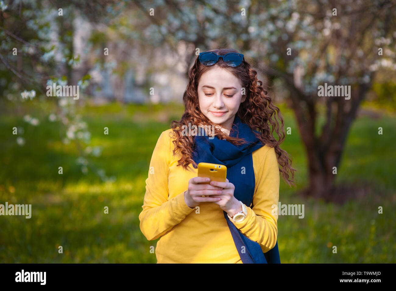 Junge smilling stehende Frau in einem blühenden Garten und schreibt auf Handy. Kirschblüten. Porträt der schönen Frau Stockfoto