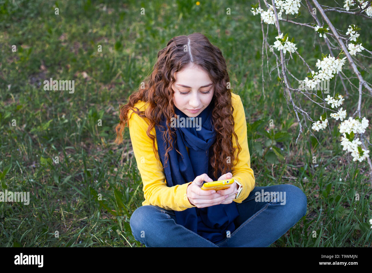 Junge smilling Frau in einem blühenden Garten sitzen und schreibt auf Handy. Kirschblüten. Portrait von schönen Mädchen Stockfoto