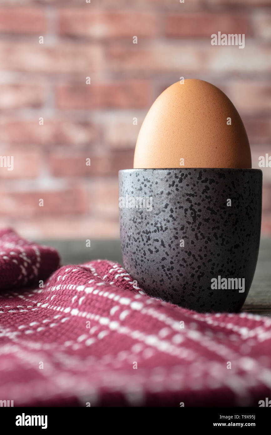 Weich gekochtes Ei in eine Tasse mit einem Geschirrtuch auf rustikalem Tisch und Backstein Hintergrund Stockfoto