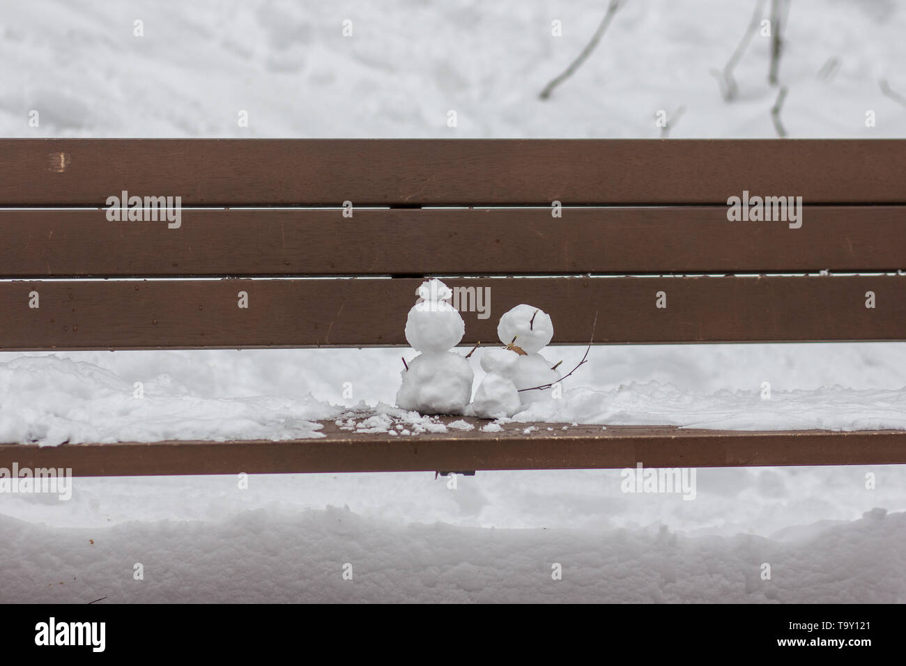 Ein Bild von einem kleinen Schneemann von zwei großen Schneemann auf einer Holzbank, begleitet. Stockfoto