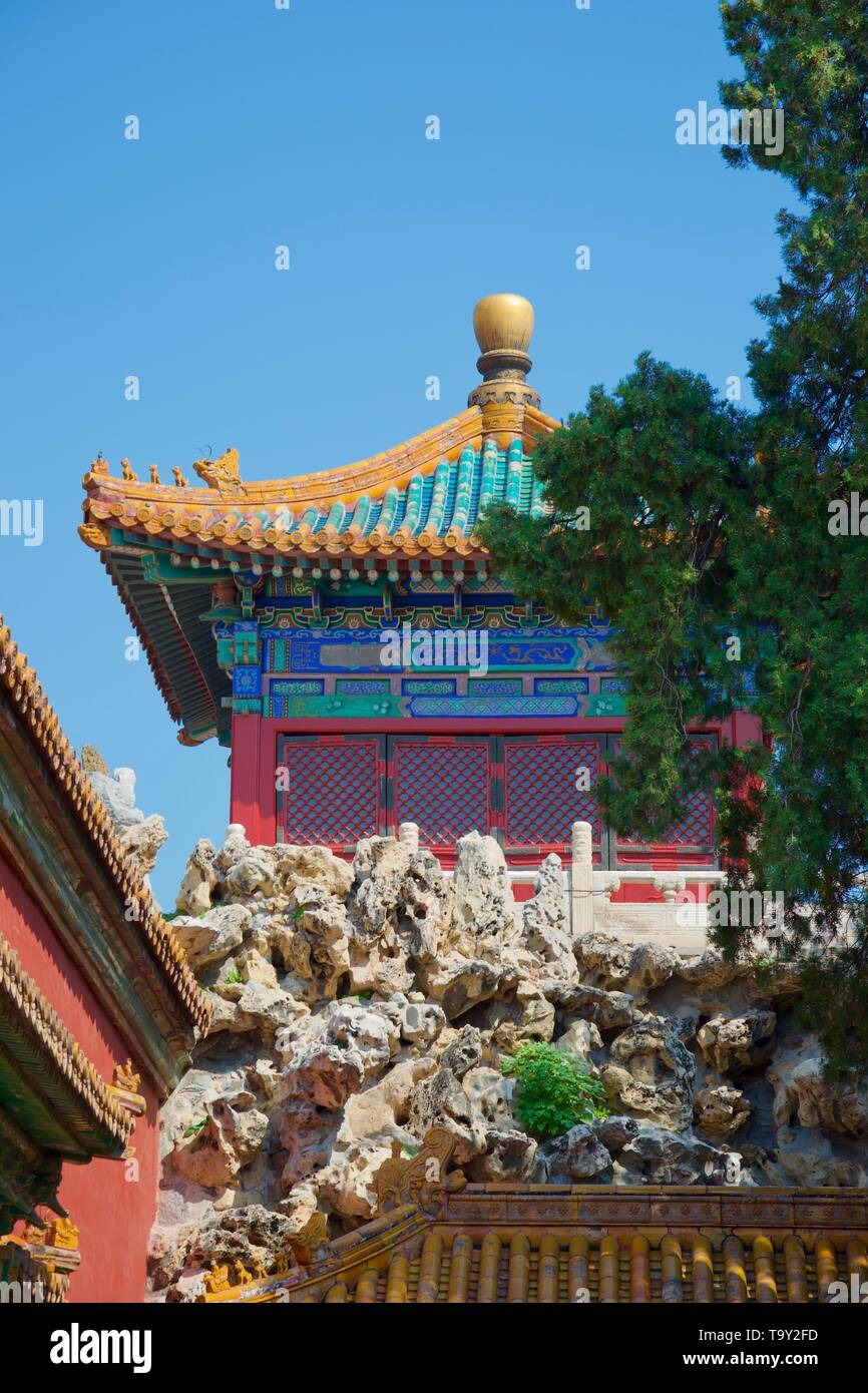 Der Sonnenbeschienenen Steingarten und Baum im Vordergrund, mit einer lebendigen, bunt bemalten Chinesischen Tempel (Pagode) in Gold, Blau, Grün und Rot gegen den hellen Himmel. Stockfoto