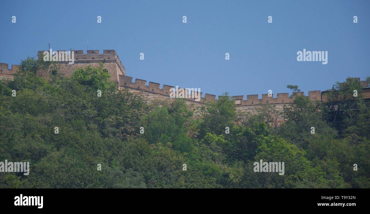 Grüne Bäume im Vordergrund und tief blauem Himmel hinter der Brüstung der Großen Mauer von China - Stein Festung gegen Skyline Stockfoto