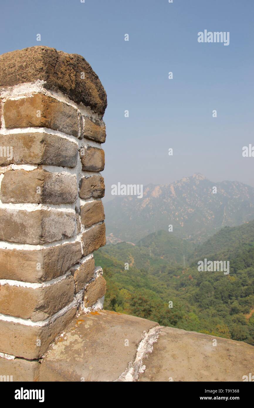 Auf einem Berg in der fernen Dunst; Fokus auf Stein crenellation der Attika der Großen Mauer von China - Mauerwerk und Mörtel. Stockfoto