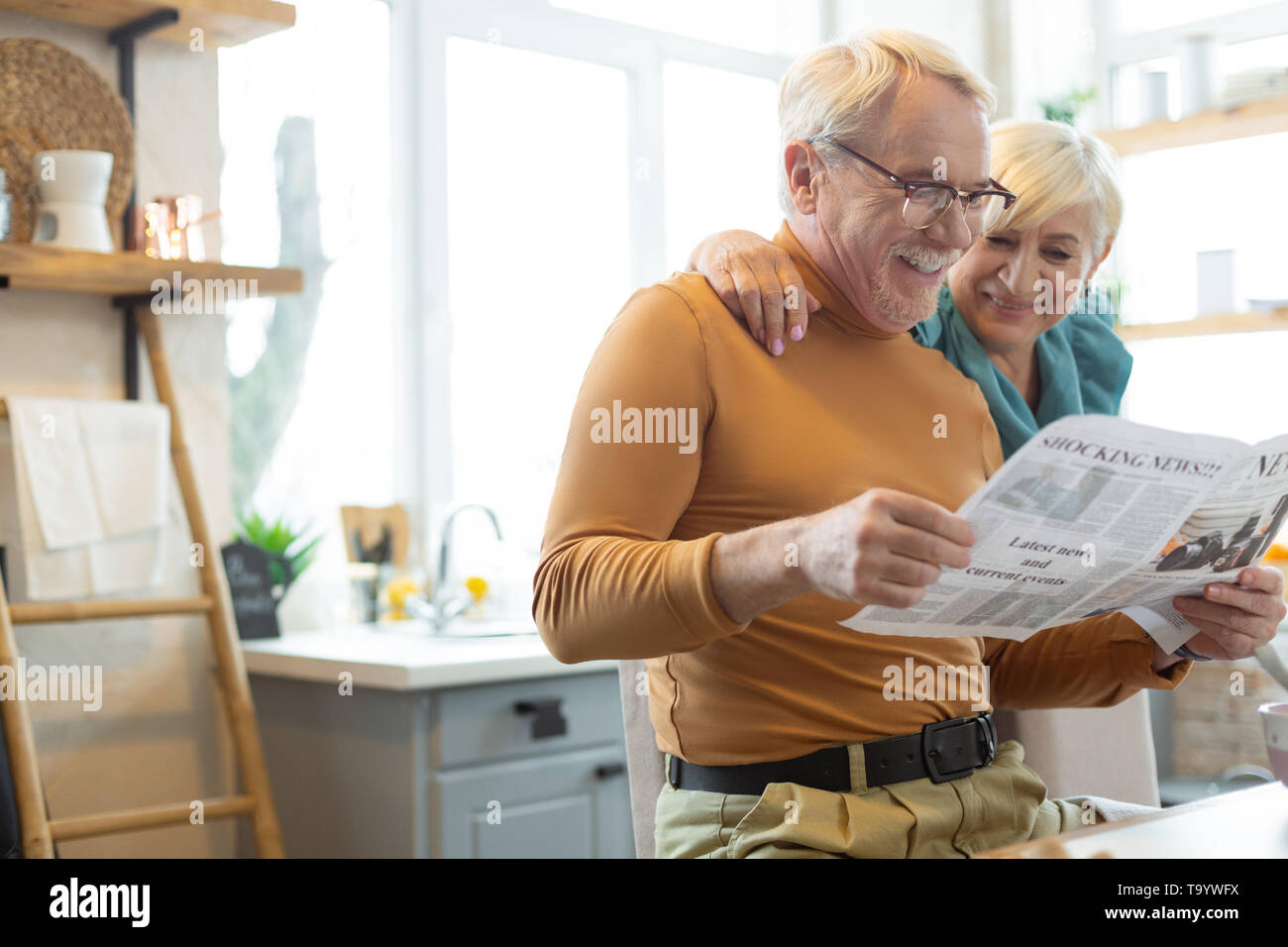 Lächelnde Menschen engagieren im Lesen, während seine Frau ihn umarmen Stockfoto