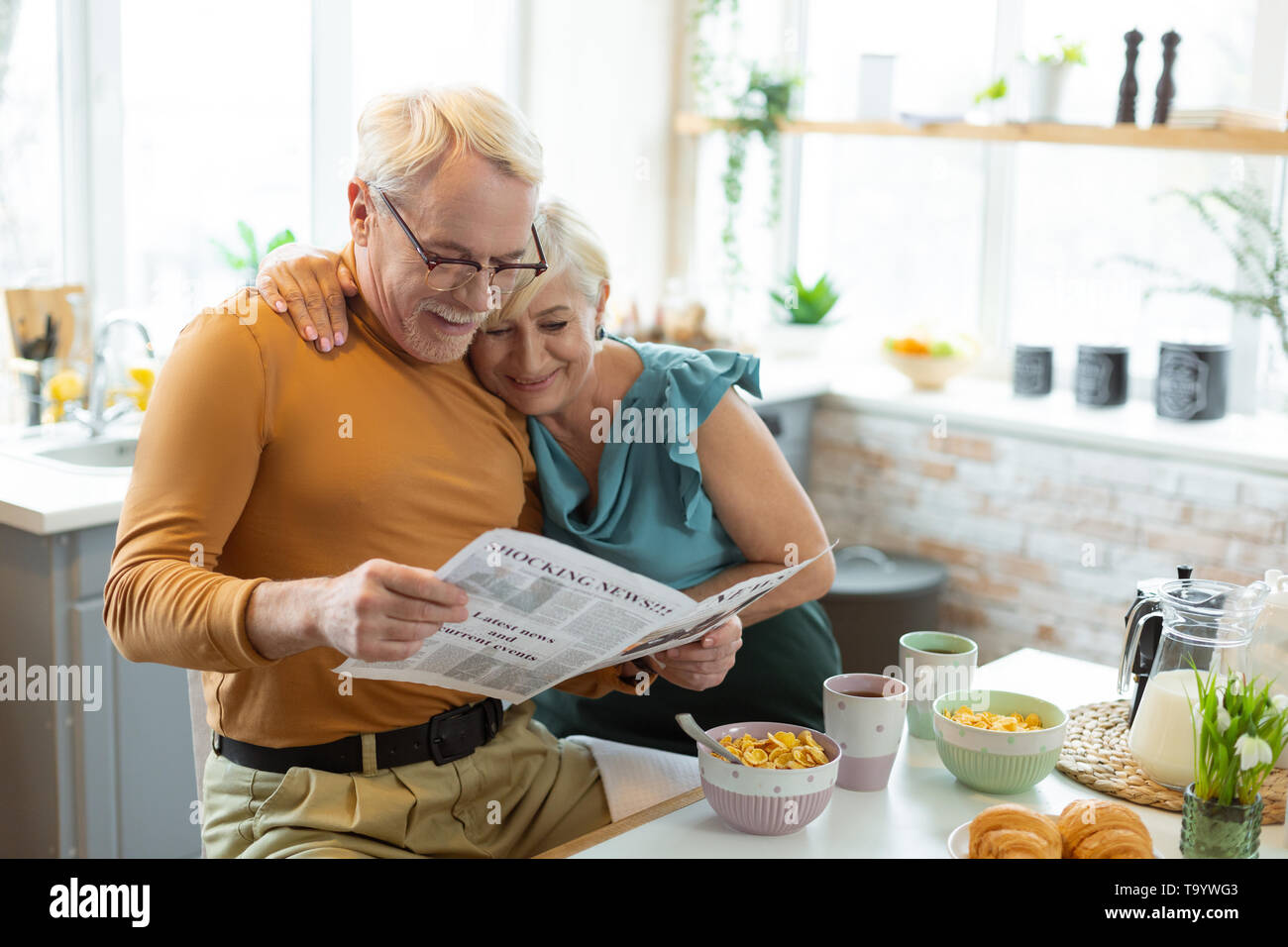 Lächelnd schöne ansprechende alter weisshaariger Ehepaar, das Lesen einer Zeitung zusammen Stockfoto