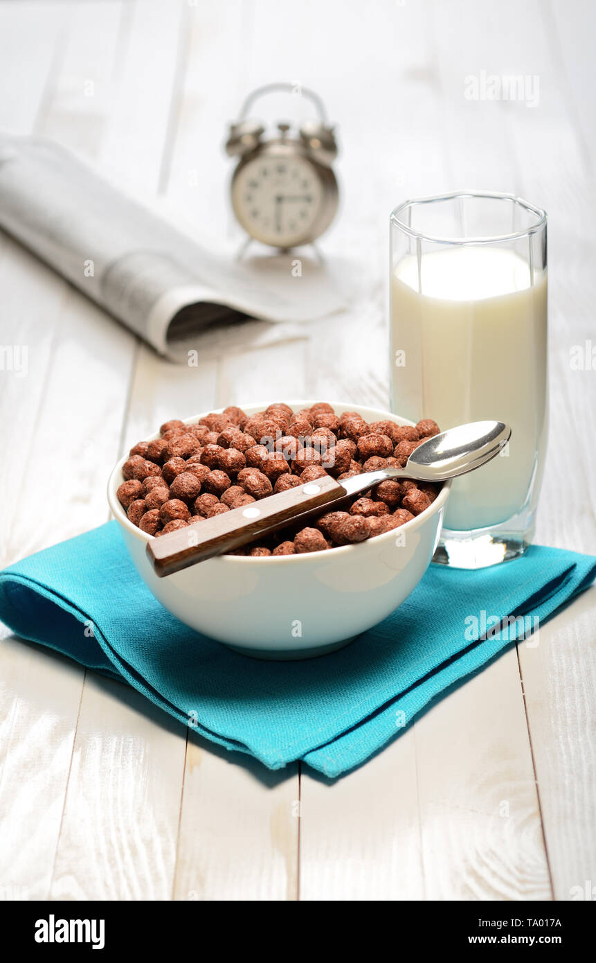 Schokolade corn flakes auf Holzbrett Tabelle mit Wecker und Zeitungen Stockfoto