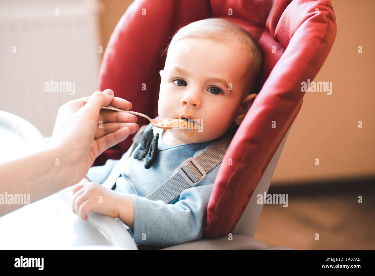 Baby essen püriert Apple vom Löffel drinnen. Mit Blick auf die Kamera. Kindheit. Stockfoto