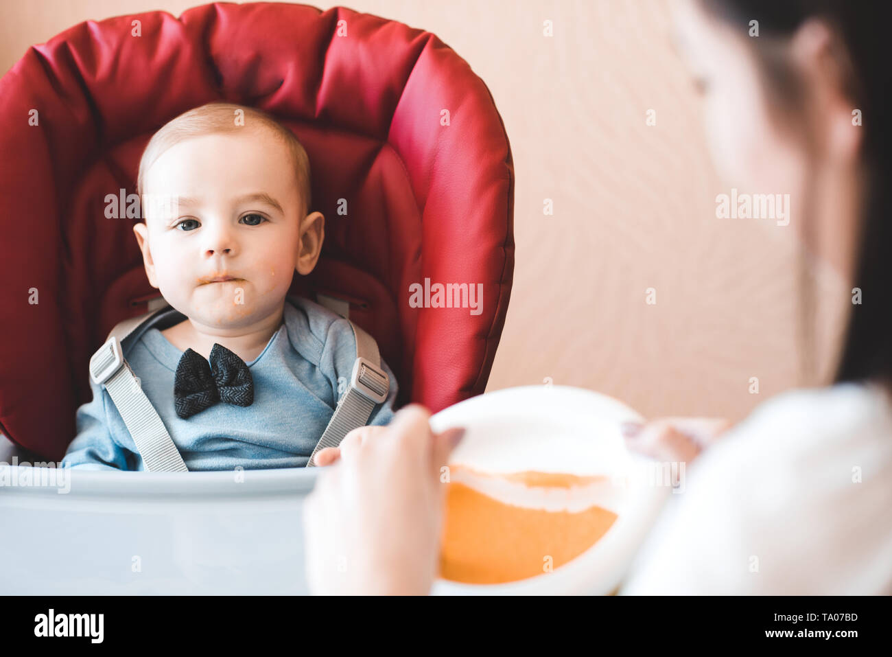 Mutter feeding baby boy in Stuhl in der Küche. Mit Blick auf die Kamera. Die Mutterschaft. Mutterschaft. Stockfoto