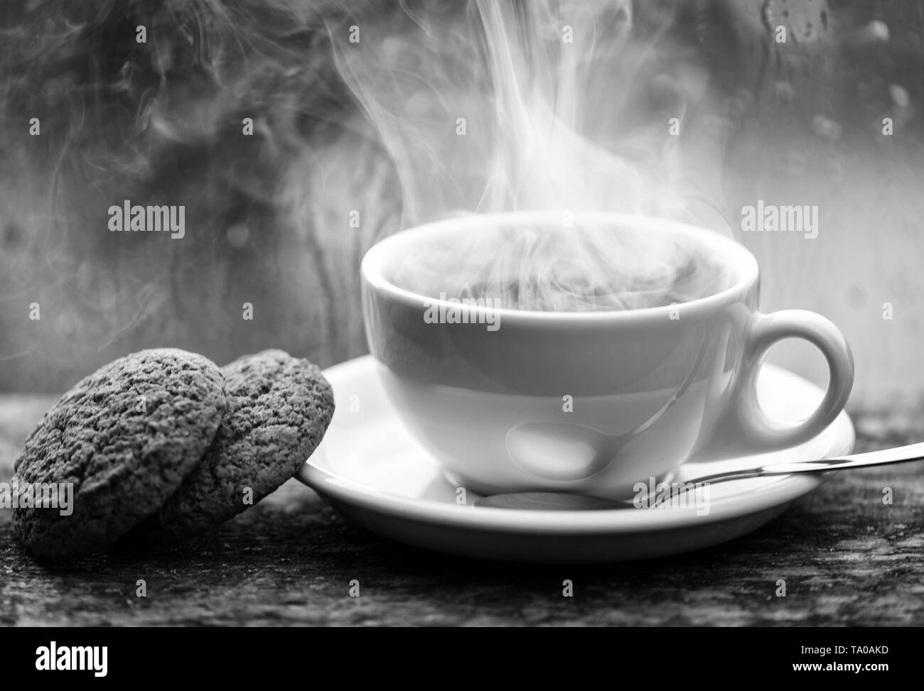 Kaffee Zeit an regnerischen Tag. Frisch gebrühter Kaffee in weiße Tasse oder Becher auf der Fensterbank. Nasses Glas Fenster und heiße Tasse Koffein trinken. Kaffee trinken mit Oat cookies Dessert. Genießen Kaffee an regnerischen Tag. Stockfoto