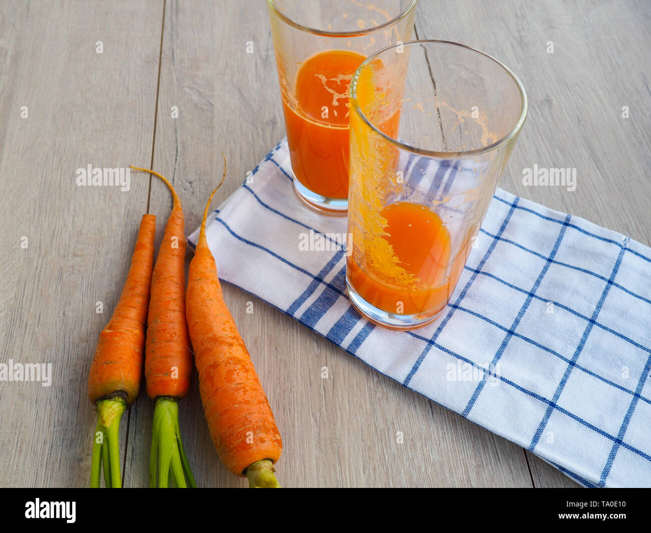 Gläser Karottensaft und frische Karotten auf Holz Schneidebrett, der Saft geklopft, das leere Glas bleibt Stockfoto