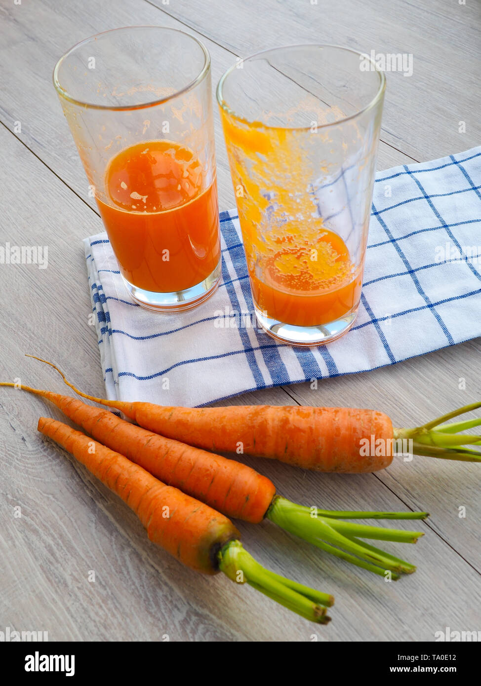 Gläser Karottensaft und frische Karotten auf Holz Schneidebrett, der Saft geklopft, das leere Glas bleibt Stockfoto