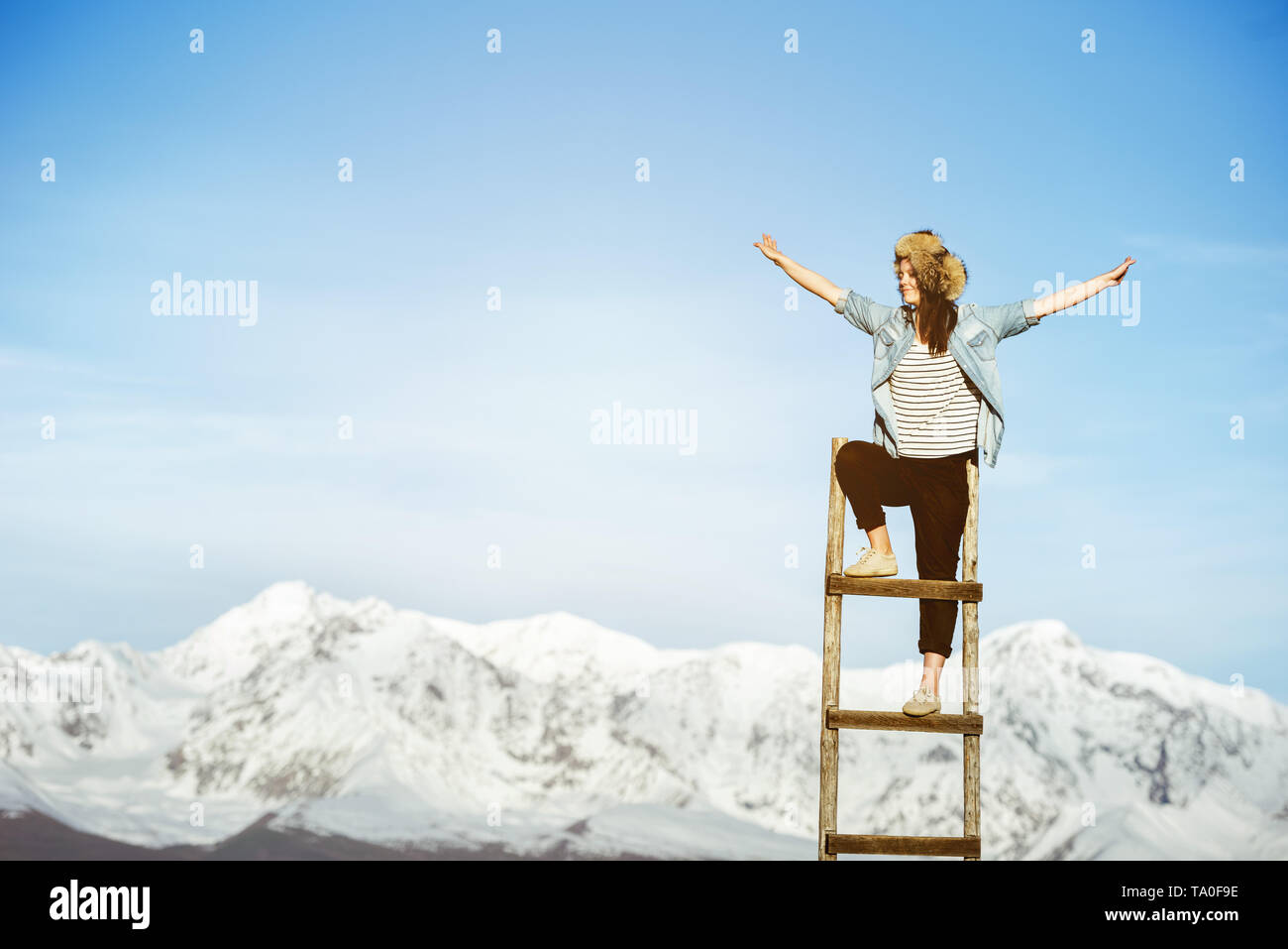 Glückliches Mädchen steht auf der Holztreppe mit erhobenen Armen gegen Snowy Mountains Stockfoto