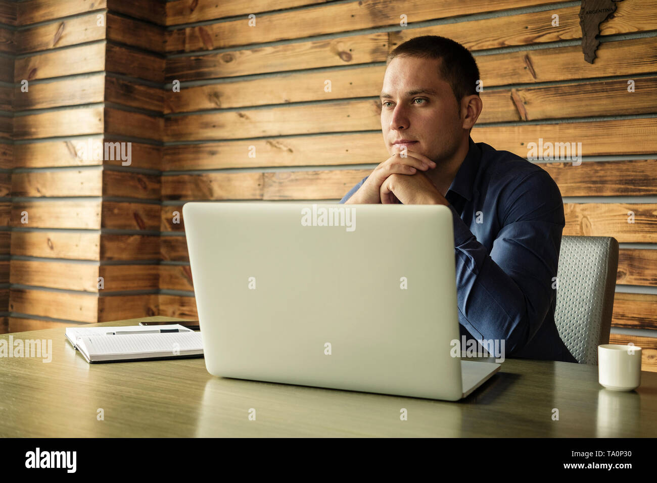 Nachdenklich Unternehmer oder Manager im Büro hinter einem Laptop mit seinem Kinn auf seine Hände vor starrte mit einem nachdenklichen Ausdruck Stockfoto