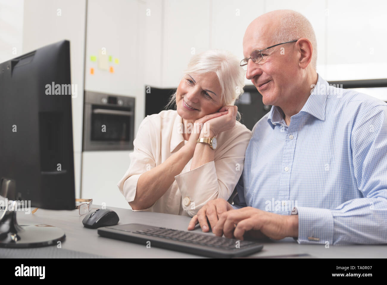 Gerne ältere Paare zusammen am Computer genießen. Senioren einen Computer benutzen, betrachten Sie die Bilder, die Sie erhalten haben. Stockfoto