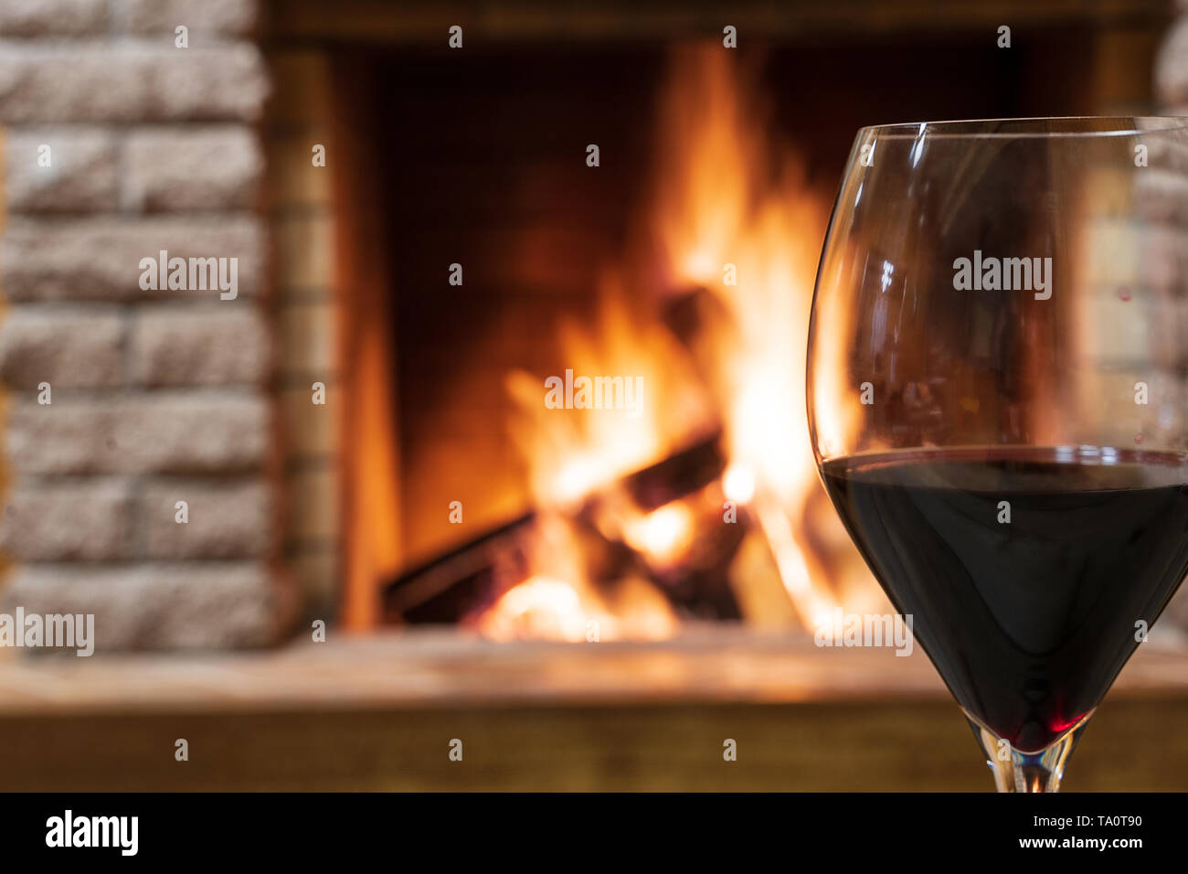 Nahaufnahme Glas Rotwein gegen gemütlichen Kamin Hintergrund, in Country House, horizontal, hygge, Home sweet home. Stockfoto
