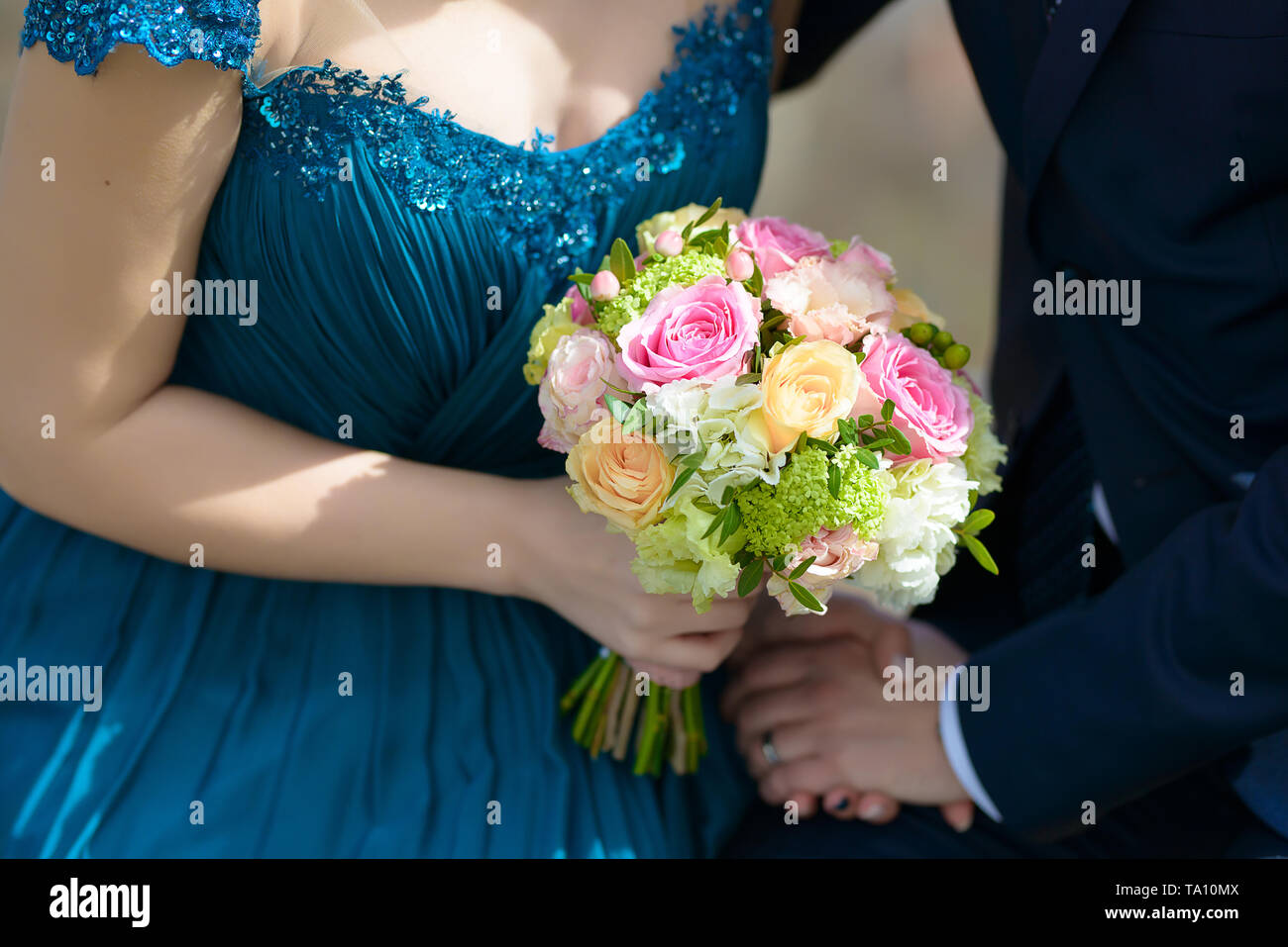 Die Braut trägt ein blaues Kleid und der Bräutigam bei der Hochzeit mit Fokus auf die Braut Hände halten ein großes rundes Bouquet mit pastellfarbenen Rosen Stockfoto