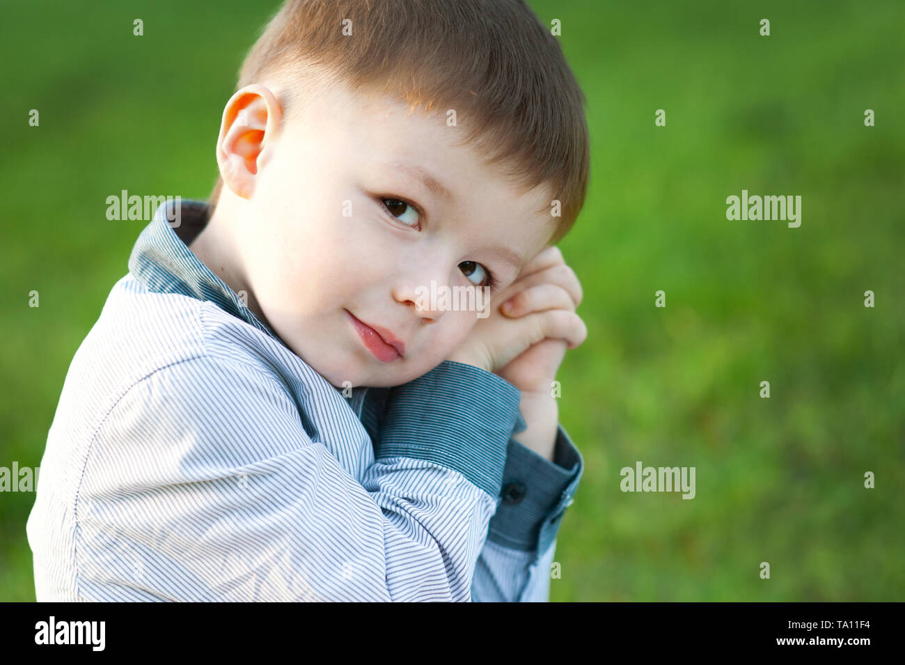 Süße Junge sitzt auf grünem Gras. Er wartet. Konzept der Kinder glücklich Stockfoto