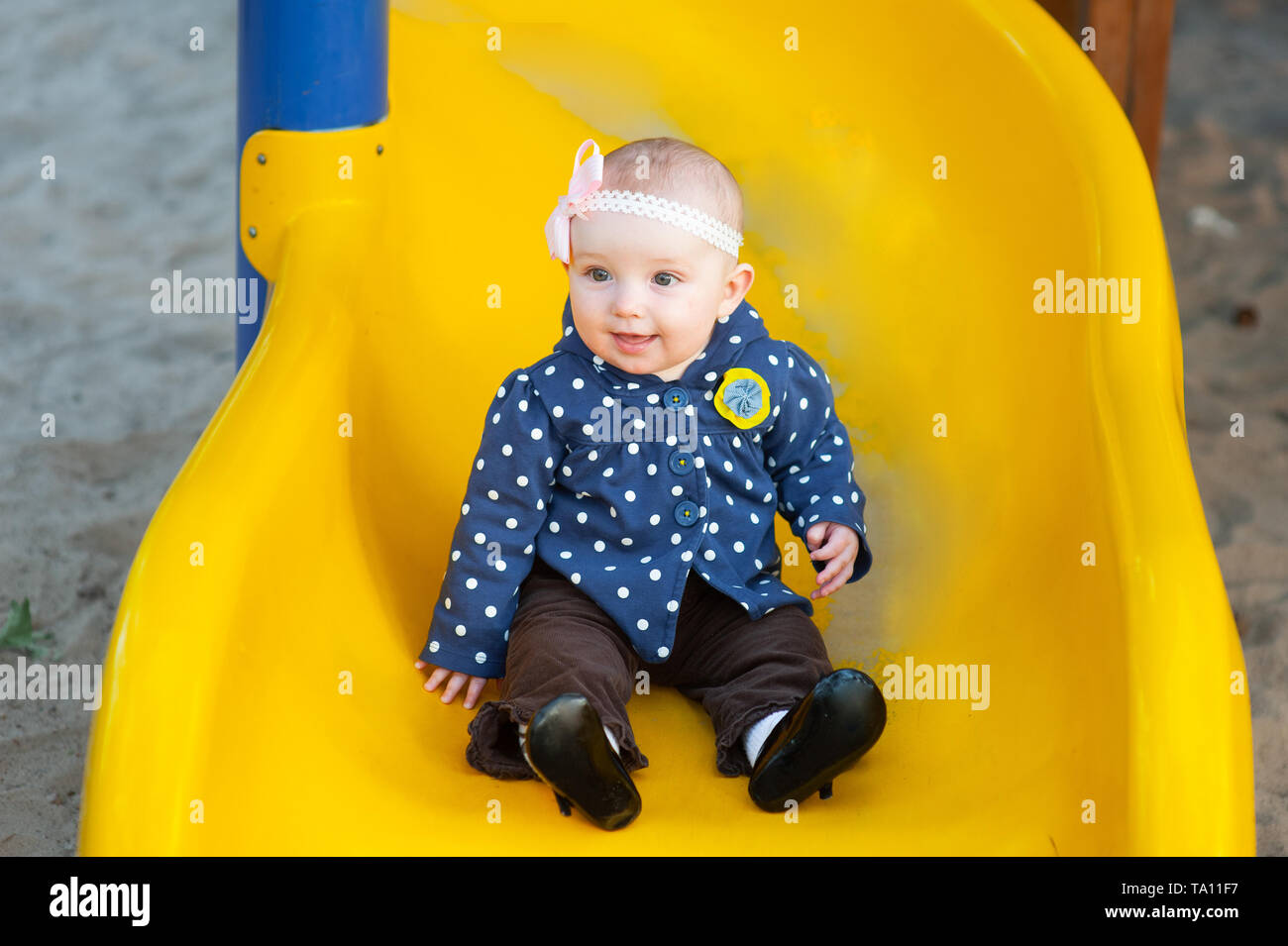 Mädchen zwei Jahre alte Brünette in Jacke reiten auf einem gelben Hügel auf dem Spielplatz im Park Stockfoto