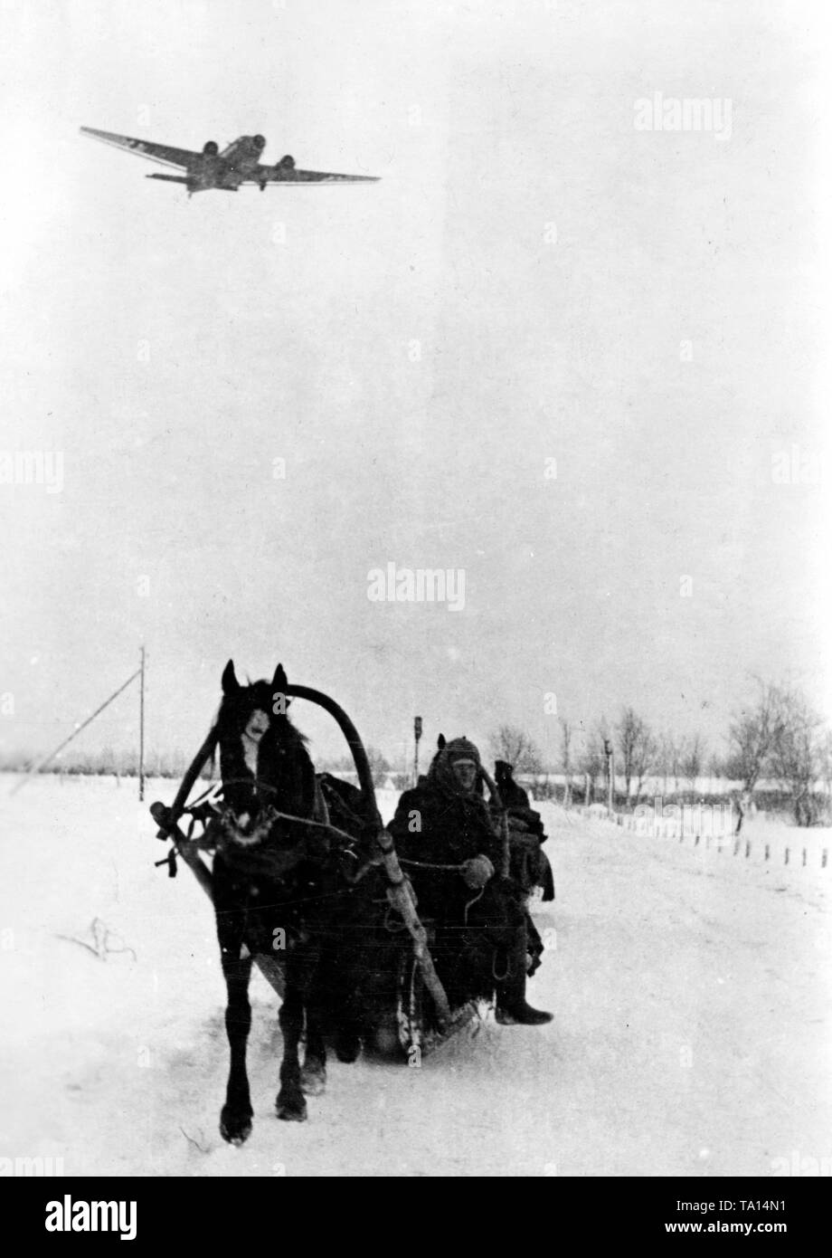 Deutsche Soldaten fahren mit dem Schlitten auf der schneebedeckten Straße in der Nähe der Stadt Demyansk. Über ihnen, einen fliegenden JU 52 (das Foto wurde im Januar 1942 aufgenommen, so dass es nicht eine partielle Flug der Luftbrücke, die den gefangenen Soldaten für fast zwei Monate in der Tasche geliefert hatte, darstellen). Foto der Propaganda Firma (PK): kriegsberichterstatter Beissel. Stockfoto