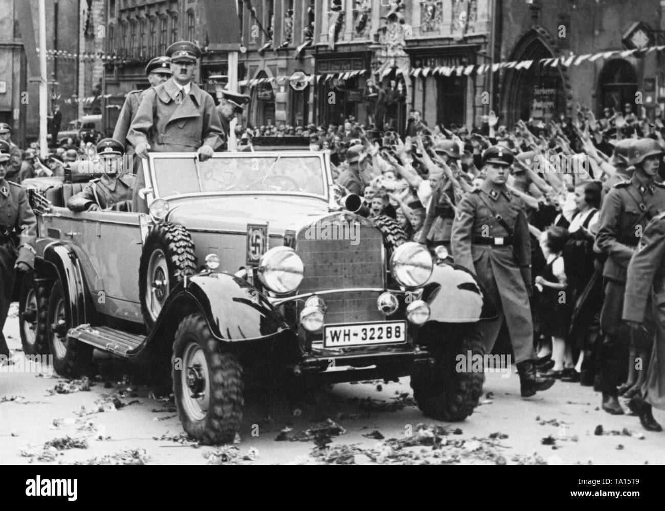 Adolf Hitler in Eger im Sudetenland. Hitlers Autokolonne durch die jubelnde Bevölkerung. Sie sind Gruß ihn mit den Hitlergruß. Adjutant Rudolf Schmundt sitzt auf der linken Seite des Autos, Bodyguards der SS sind zu Fuß neben dem Wagen. Stockfoto