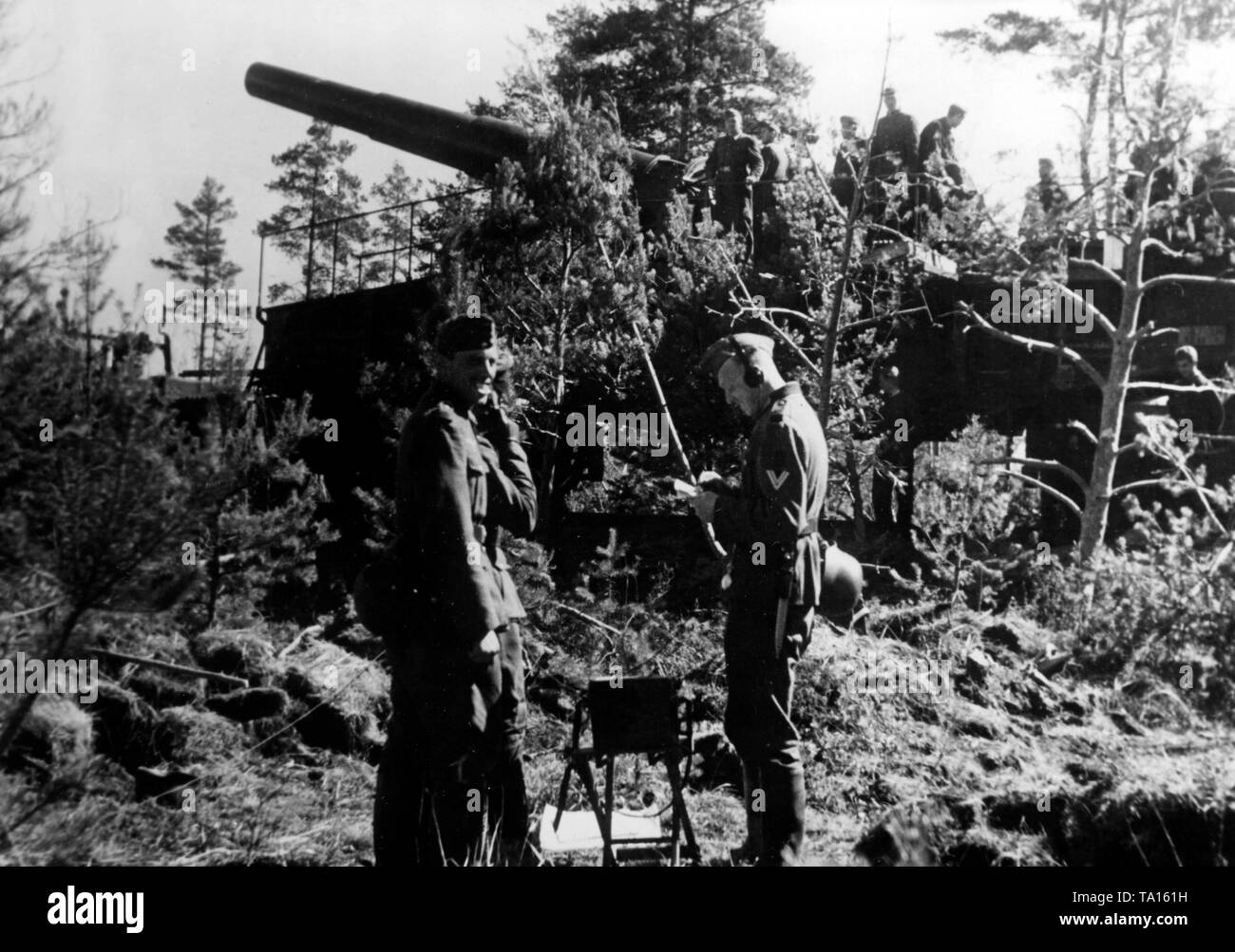 Deutsche Soldaten den Krieg Lage auf einem Feld Telefon besprechen. Im Hintergrund, andere Soldaten auf einem Railroad gun 28-cm-Kanone 5 (E), mit dem Sie von der umgebenen Stadt gefeuert. Foto der Propaganda Firma (PK): SS Kriegsberichterstatter Raudies. Stockfoto