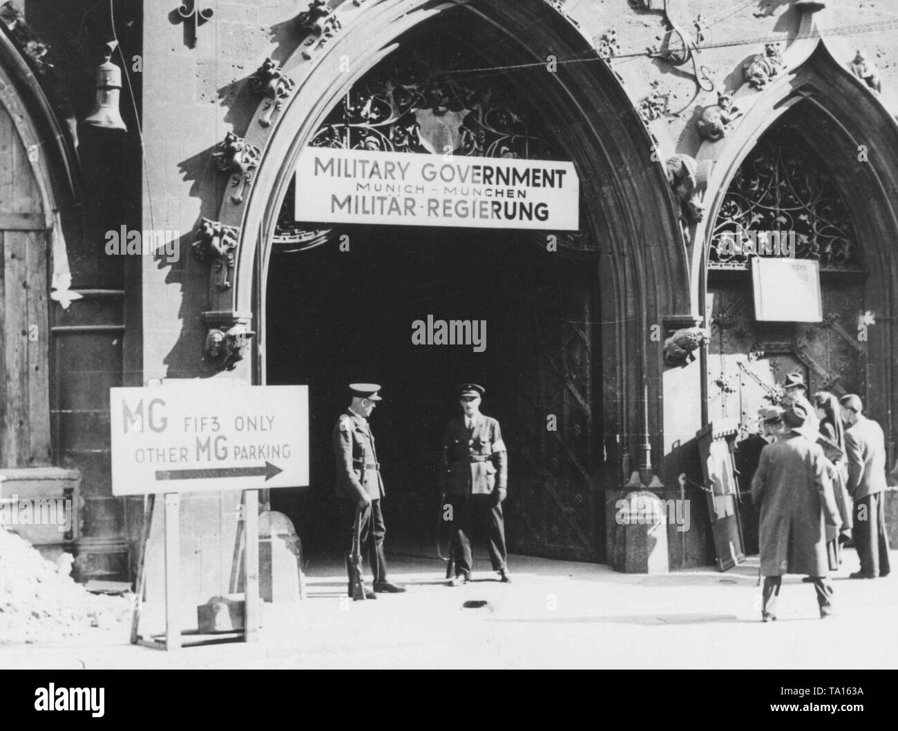 Zwei deutsche Polizisten sind Wache vor dem Münchner Rathaus, dem Sitz der amerikanischen Militärregierung. Über dem Eingang hängt ein Schild "militärische Regierung München - München Militär-Regierung'. Stockfoto