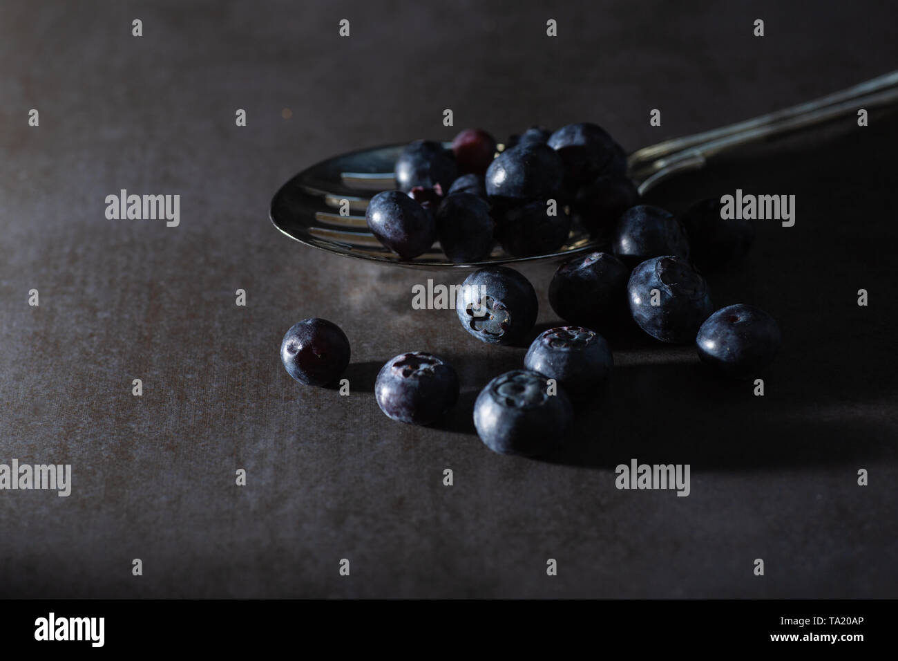 Low Key Blaubeeren auf einem vintage Löffel und dunkelgrauem Hintergrund. Stilvolles, modernes frisches Bild der gesunden superfood Obst. Horizontale. Stockfoto