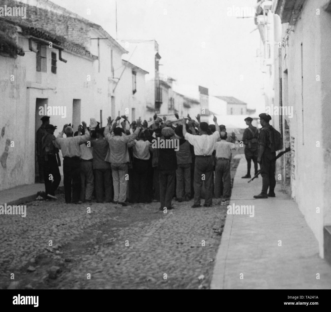 Republikanische Unterstützer der Regierung sind gemeinsam mit erhobenen Händen von spanischen Soldaten in einer kleinen Straße in einem Dorf in der Nähe von Sevilla getrieben. Stockfoto