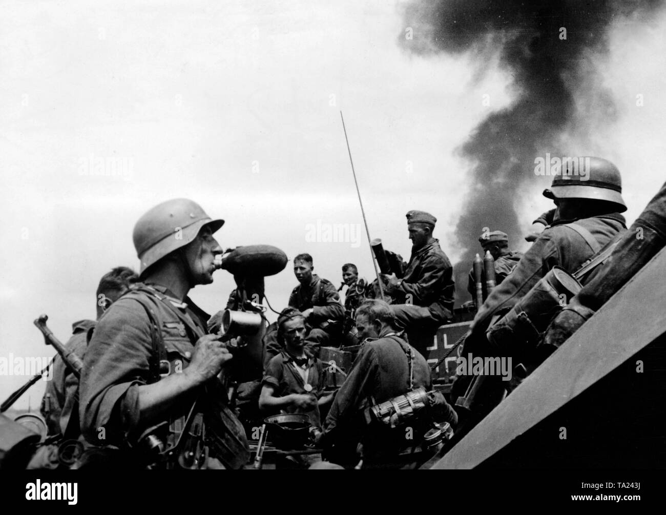 Deutsche Infanteristen während einer Pause bei den Dreharbeiten für einen Brückenkopf über den Donez. Im Hintergrund dunkler Rauch aufsteigt, im Vordergrund ein Soldat mit einer Maschine Pistole nimmt einen Schluck aus seiner Flasche. Im Hintergrund ein Sturmgeschuetz III. Kriegsberichterstatter: Kipper. Stockfoto