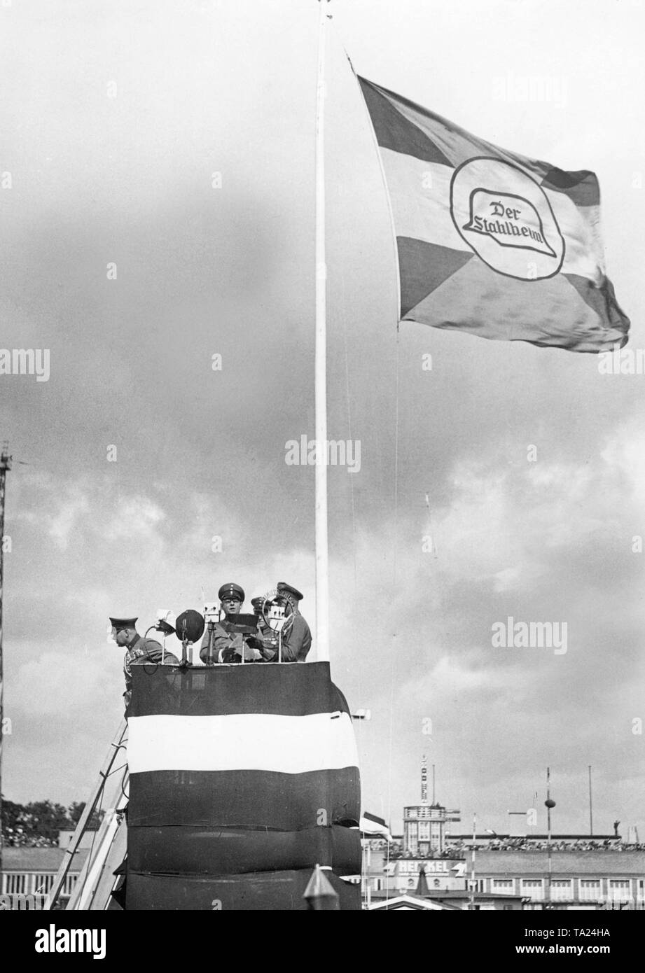 Auf dem Tempelhofer Feld der Stahlhelm hält eine Demonstration, bei der eine Rede in mehreren Mikrofonen von einem Turm gehalten wird - wie Podium. Das Podium ist dekoriert mit der schwarz-weiß-rote Flagge des Reiches, an einem Fahnenmast ist eine Fahne mit dem Symbol des Stahlhelm. Stockfoto