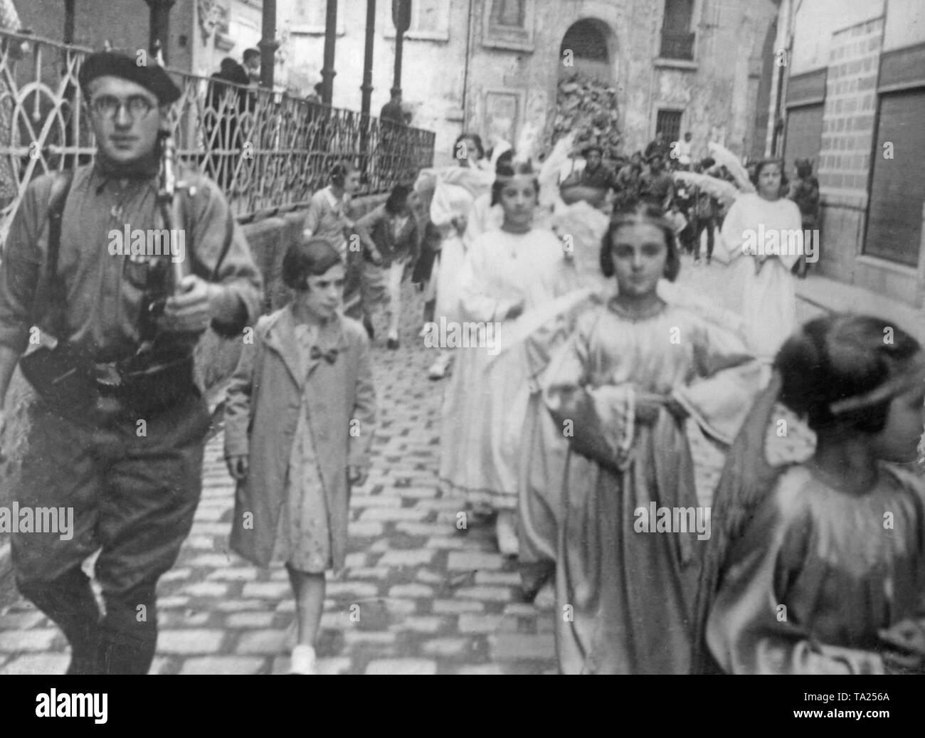 Foto von einer Prozession von Mädchen als Engel in den ersten Monaten nach Ausbruch des Spanischen Bürgerkriegs im Sommer 1936 bekleidet. Die Prozession wird von einem spanischen nationalen Kämpfer mit einer Baskenmütze und einem Geschulterten Karabiner begleitet. Stockfoto
