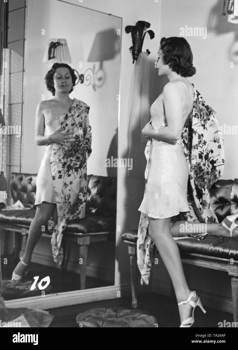 Heli Finkenzeller, eine deutsche Bühnen- und Filmschauspielerin, steht vor dem Spiegel in einem kurzen Hemd und ein morgen Kleid mit großen Blüten. Wahrscheinlich aus einer Filmszene. Stockfoto