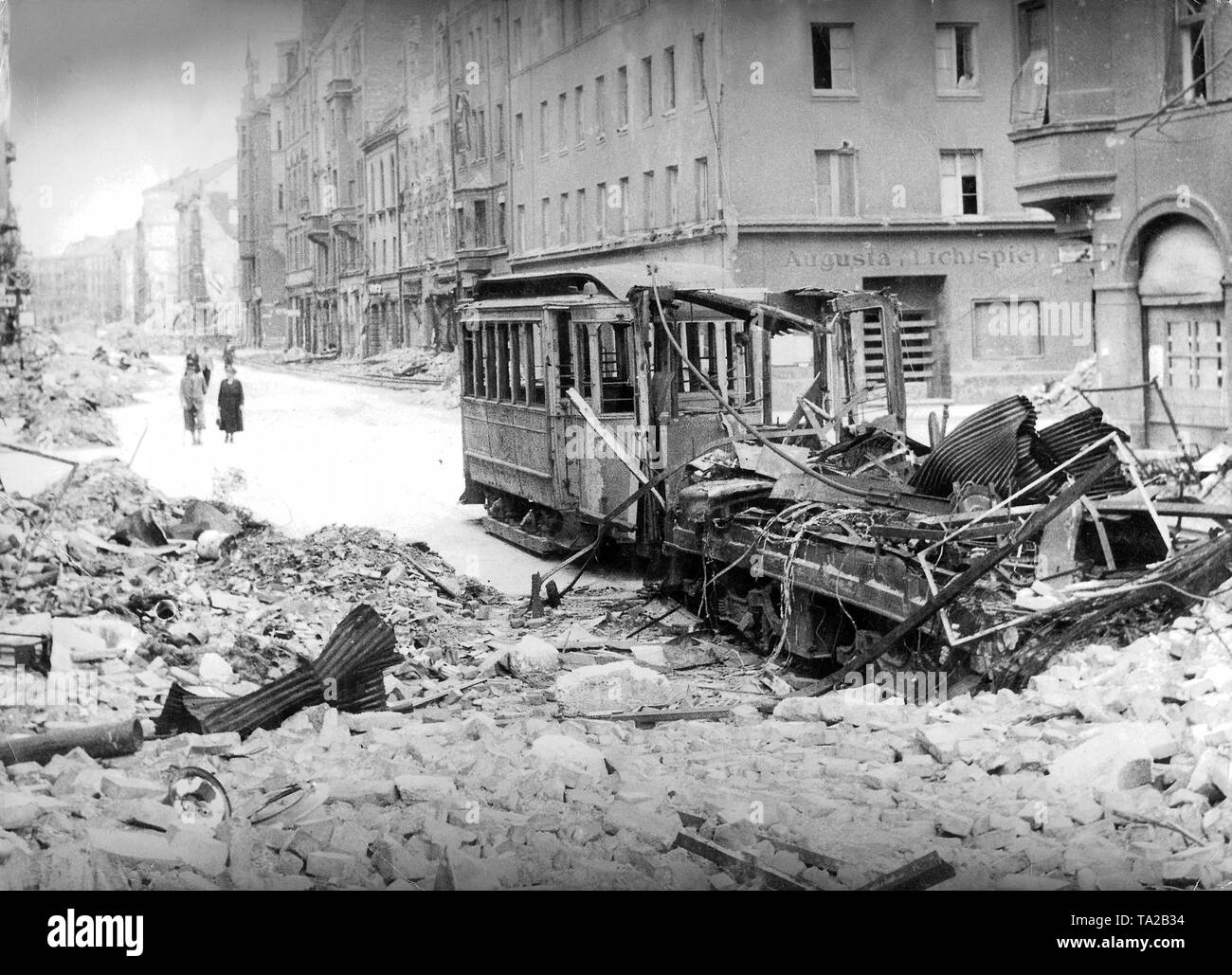 Weltkrieg II: Fußgänger in der Augustenstrasse, die voller Schutt ist. Im Vordergrund steht eine zerstörte Straßenbahn. Rechts im Hintergrund, ein Haus mit der Aufschrift 'Augusta Lichtspiele". Stockfoto