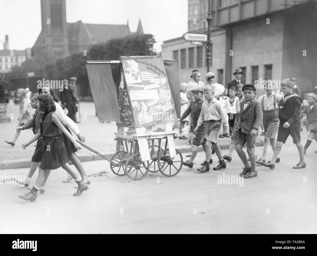 Kinder ziehen einen kleinen Wagen mit Poster und Banner der KPD (Kommunistische Partei Deutschlands). Auf dem Plakat sind die Sätze "Was Sie den Reichstag gebracht.' und 'Für einen sowjetischen Deutschland'. Stockfoto