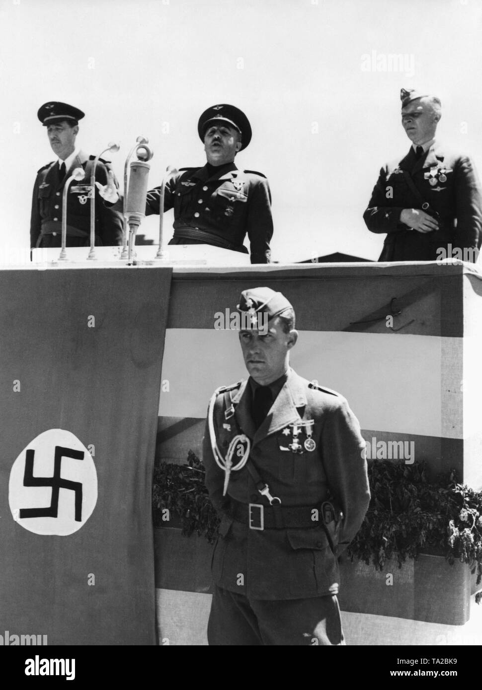 Foto der Caudillo General Francisco Franco zu einem Rednerpult während eine Adresse der Legion Condor anlässlich einer Siegesparade in Burgos, Kastilien und Leon, am 23. Mai 1939. Von links nach rechts: die spanische Luftwaffe Allgemein, Alfredo Kindelan Duany, Franco, Kommandant der Legion Condor, Major General Wolfram Freiherr von Richthofen. Unter dem Rednerpult steht ein zum Ersten Offizier der Ehrenlegion. Neben ihm, eine Hakenkreuzfahne. Stockfoto