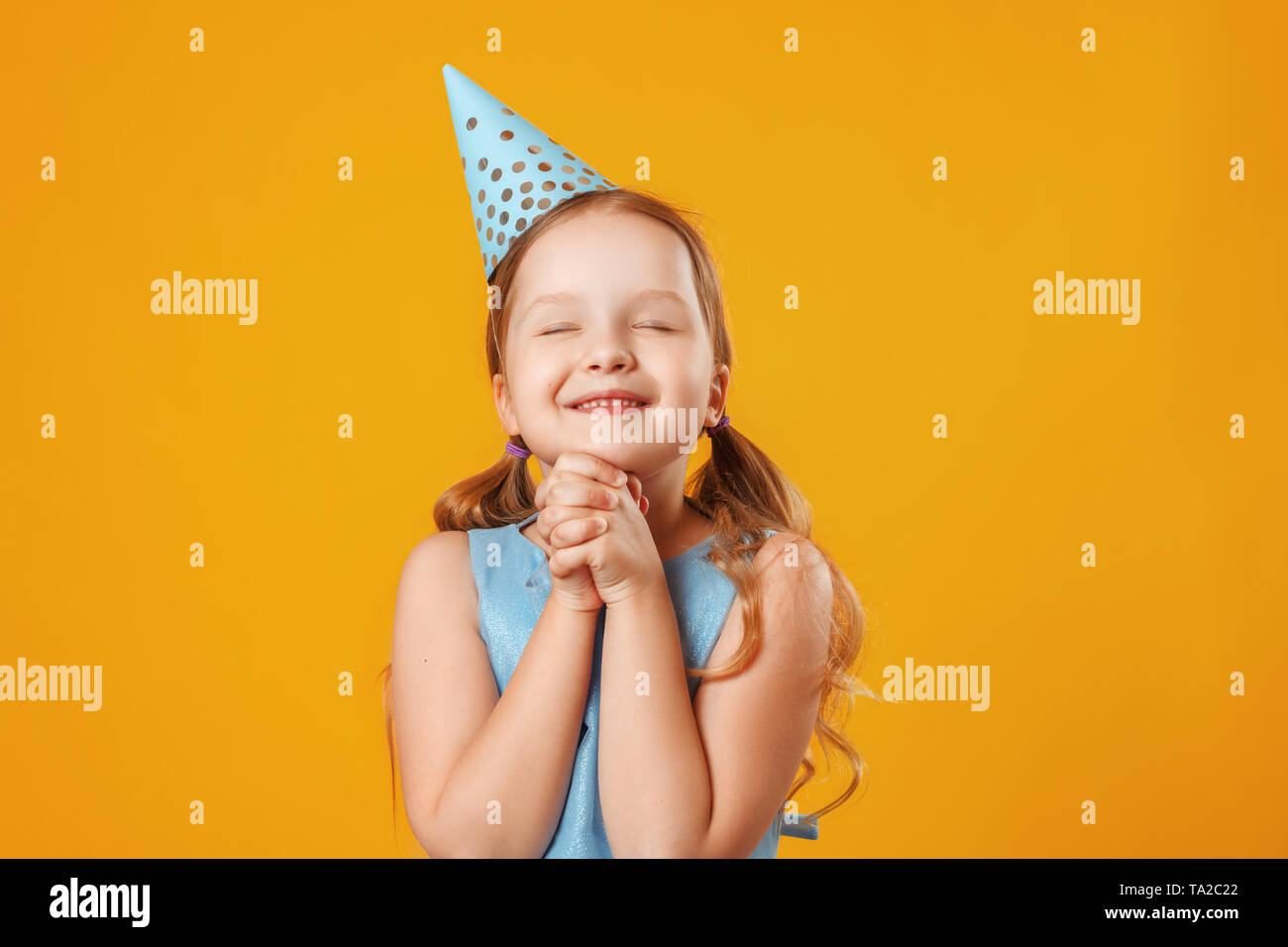 Süße kleine Mädchen feiert Geburtstag. Das Kind schloss die Augen und machte einen Wunsch. Closeup Portrait auf gelben Hintergrund. Stockfoto