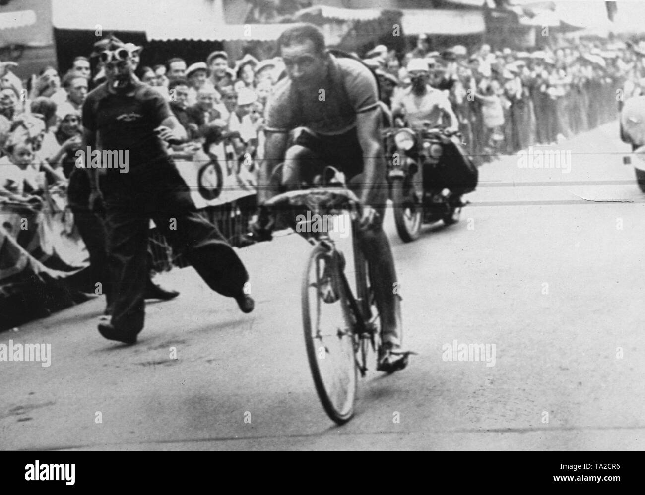 Französische Radfahrer Roger Lapebie auf der 9. Etappe der Tour de France 1937 in Digne-les-Bains. Er gewann diese Phase und die Tour de France. Ein Zuschauer läuft neben dem Radfahrer. Stockfoto