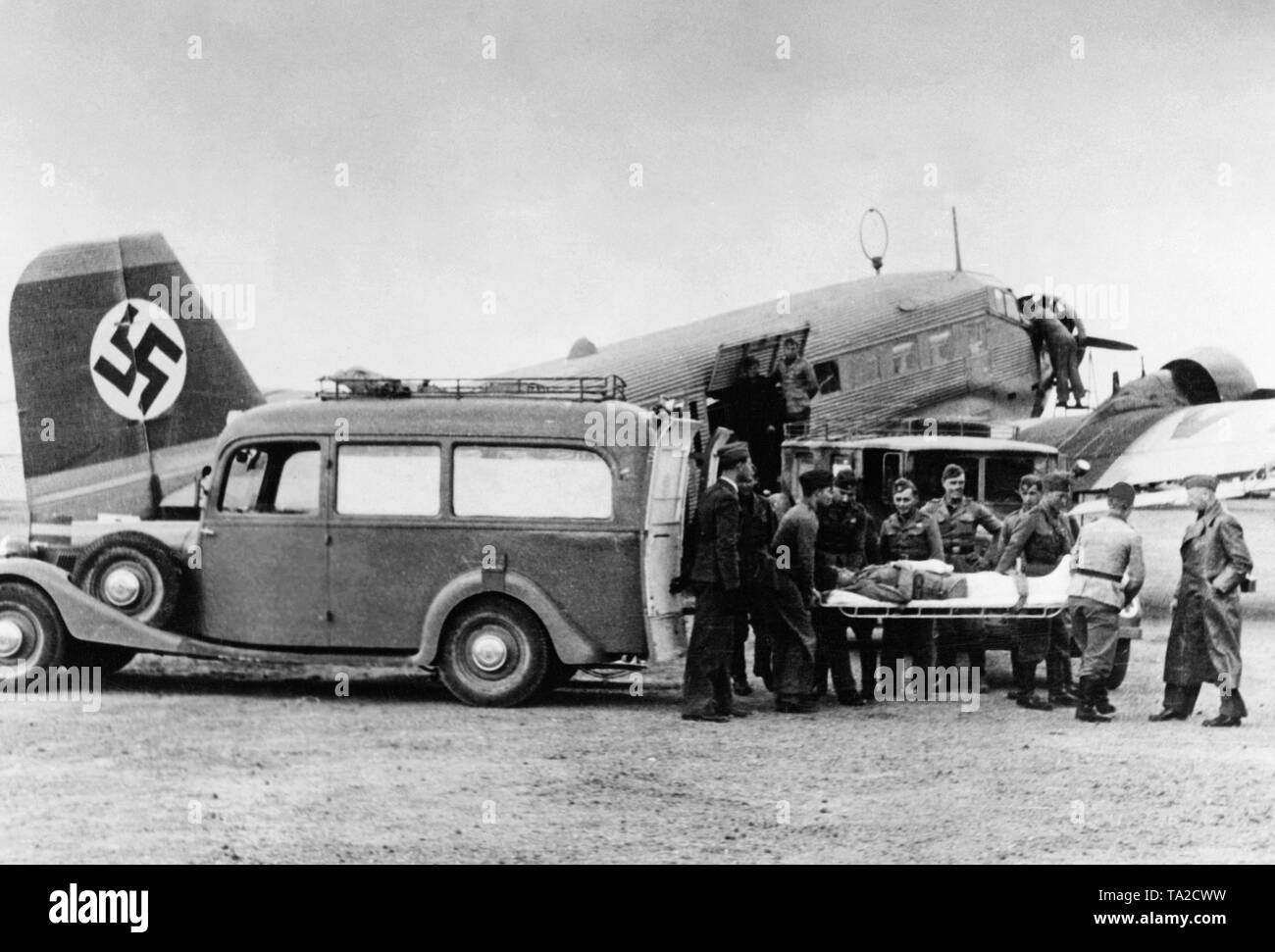 Foto eines verwundeten Soldaten der Legion Condor, die von Kameraden auf einer Bahre aus einem Krankenwagen Auto einen Air Ambulance gebracht wird (Junkers Ju 72) der Deutschen Lufthansa. Ein großes Hakenkreuz auf der vertikalen Schwanz angezeigt. Stockfoto