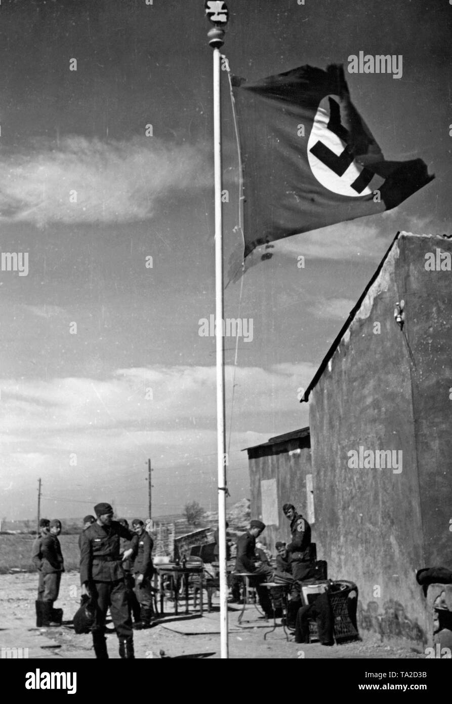 Foto von einem Fahnenmast mit einem Hakenkreuz der Bomber squadron der Bekämpfung der Gruppe 88 auf einem Flugplatz. Im Hintergrund, Soldaten des Geschwaders. An der Spitze der Fahnenstange das geschwader Abzeichen (Eagle Durchführung Sturzflug mit Bombe, hull kokarde). Stockfoto