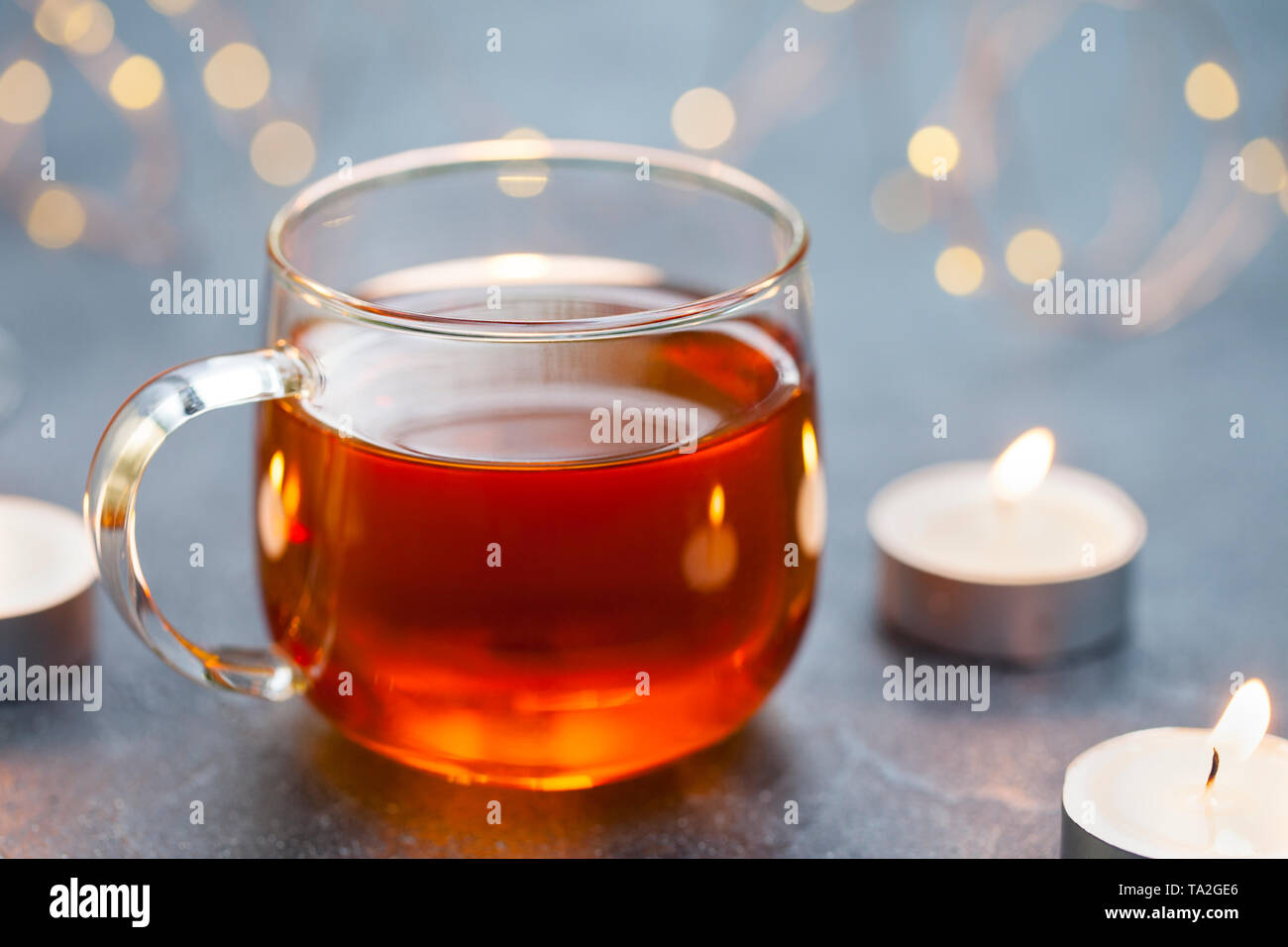 Schwarzer Tee im Glas Schale mit Kerzen und Licht Girlande. Grauer Hintergrund. Kopieren Sie Platz. Stockfoto