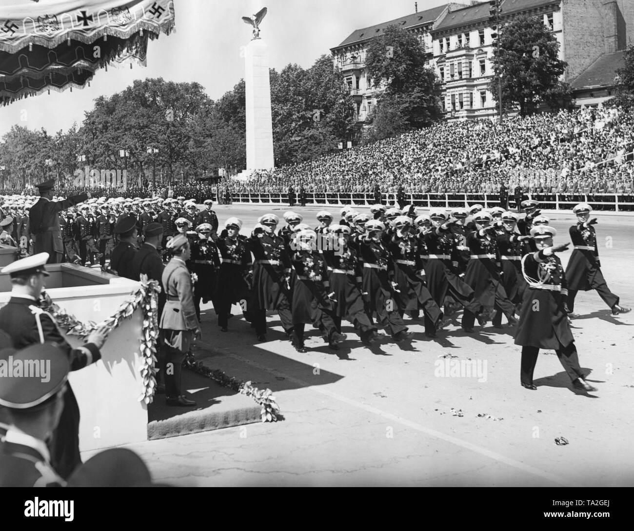 Foto eines marine Formation (die Offiziere geben den Hitlergruss) marschieren vor der Offiziere der Wehrmacht und Führer, Adolf Hitler (unter einem Vordach), bei der Parade der Legion Condor auf der Ost-West-Achse (ehemalige Chalottenburger Chaussee, heute Straße des 17. Juni) vor der Technischen Universität am 6. Juni 1939. Stockfoto