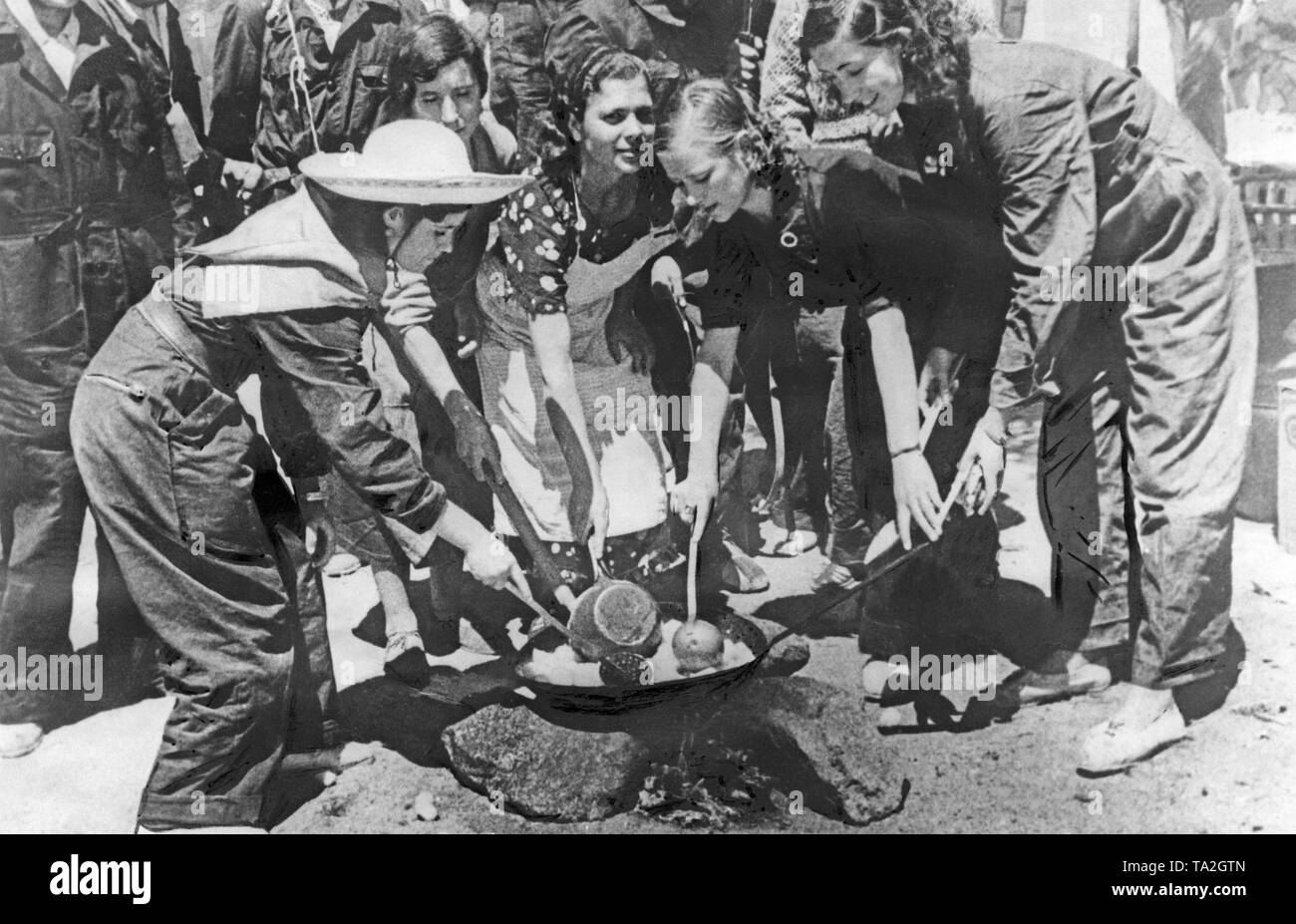 Foto von einer Gruppe von Republikanischen Kämpferinnen in ziviler Kleidung und blauen Overall Kochen am offenen Feuer. Die Frauen zusammen in die Pfanne rühren. Das Foto wurde hinter der Front in der Sierra Guadarrama. Stockfoto